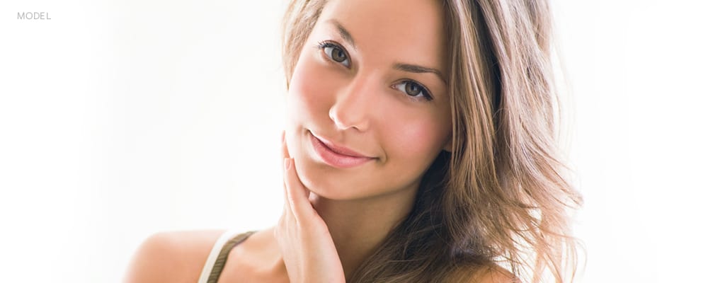 Headshot of Young Brunette Woman Softly Smiling with Hand Rubbing her Face