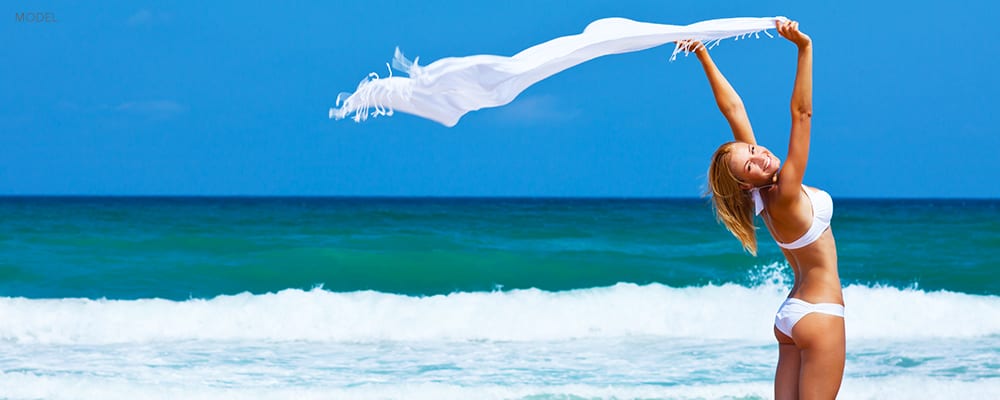 Happy Woman in Bikini Holding up Shawl Blowing in the wind on a Beach